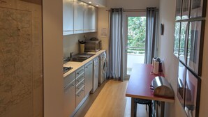 Une cuisine moderne dotée d’appareils électroménagers en acier inoxydable, un coin repas avec une table et des chaises, et une vue à travers la porte vitrée.