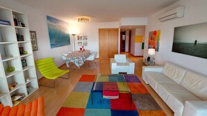 Un salon moderne avec un canapé blanc, un tapis coloré, une table à manger avec des chaises et une bibliothèque.
