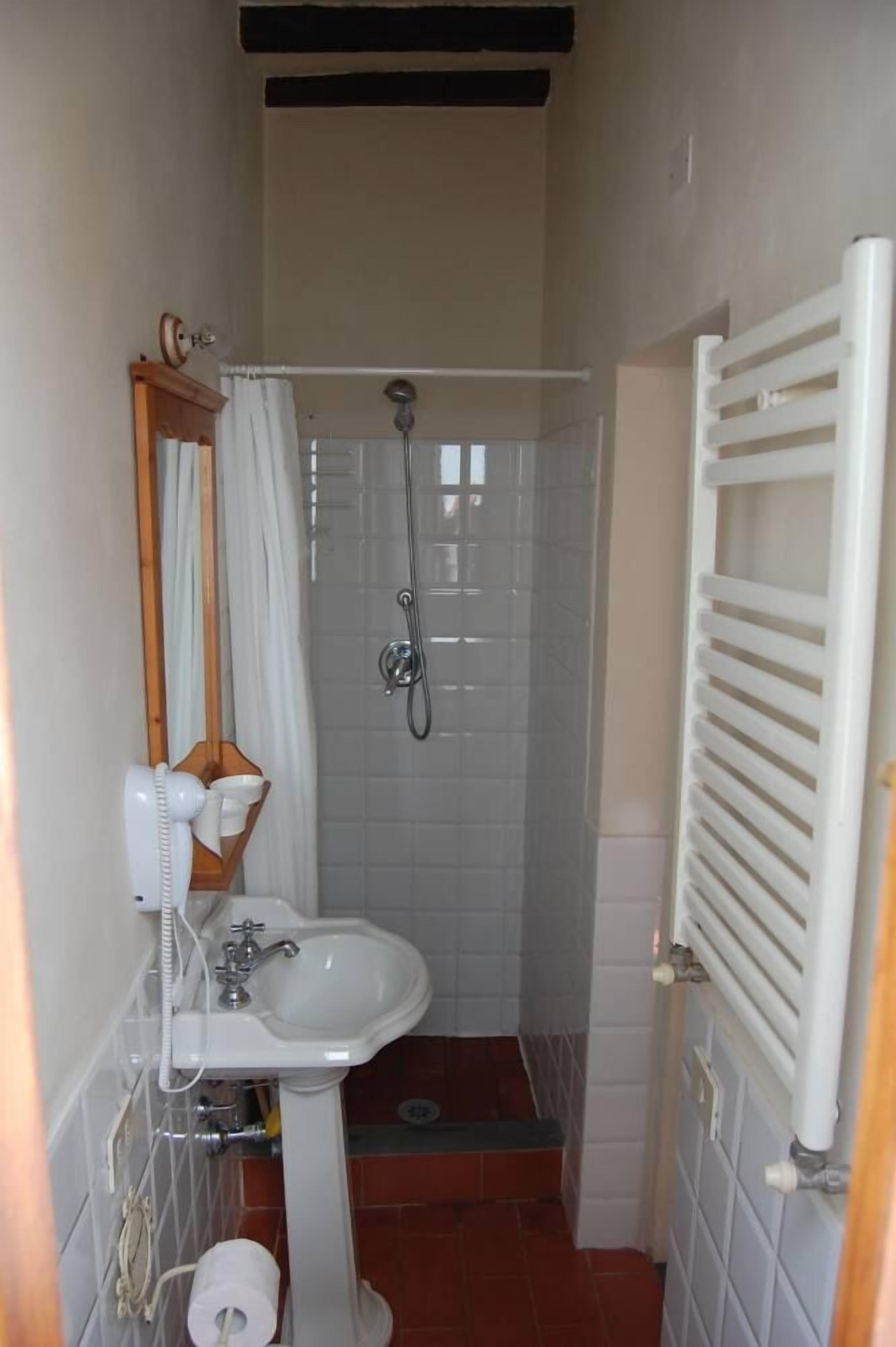 A compact bathroom with a pedestal sink, a shower enclosure, a towel rack, and a toilet.