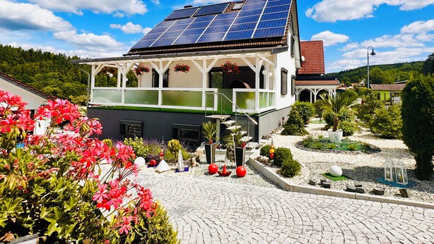 A house with solar panels, a balcony, and a garden with red flowers. - Nestled between Rennsteig and the UNESCO Biosphere Reserve Thuringian Forest (Nahetal-Waldau)