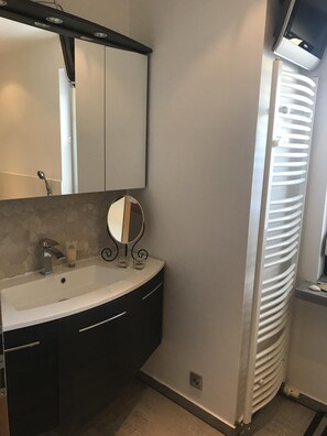 A bathroom with a white sink, dark cabinets, a mirror, and a white towel warmer.