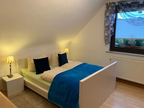 A bedroom with a bed, bedside lamps, a window with curtains, and a radiator.