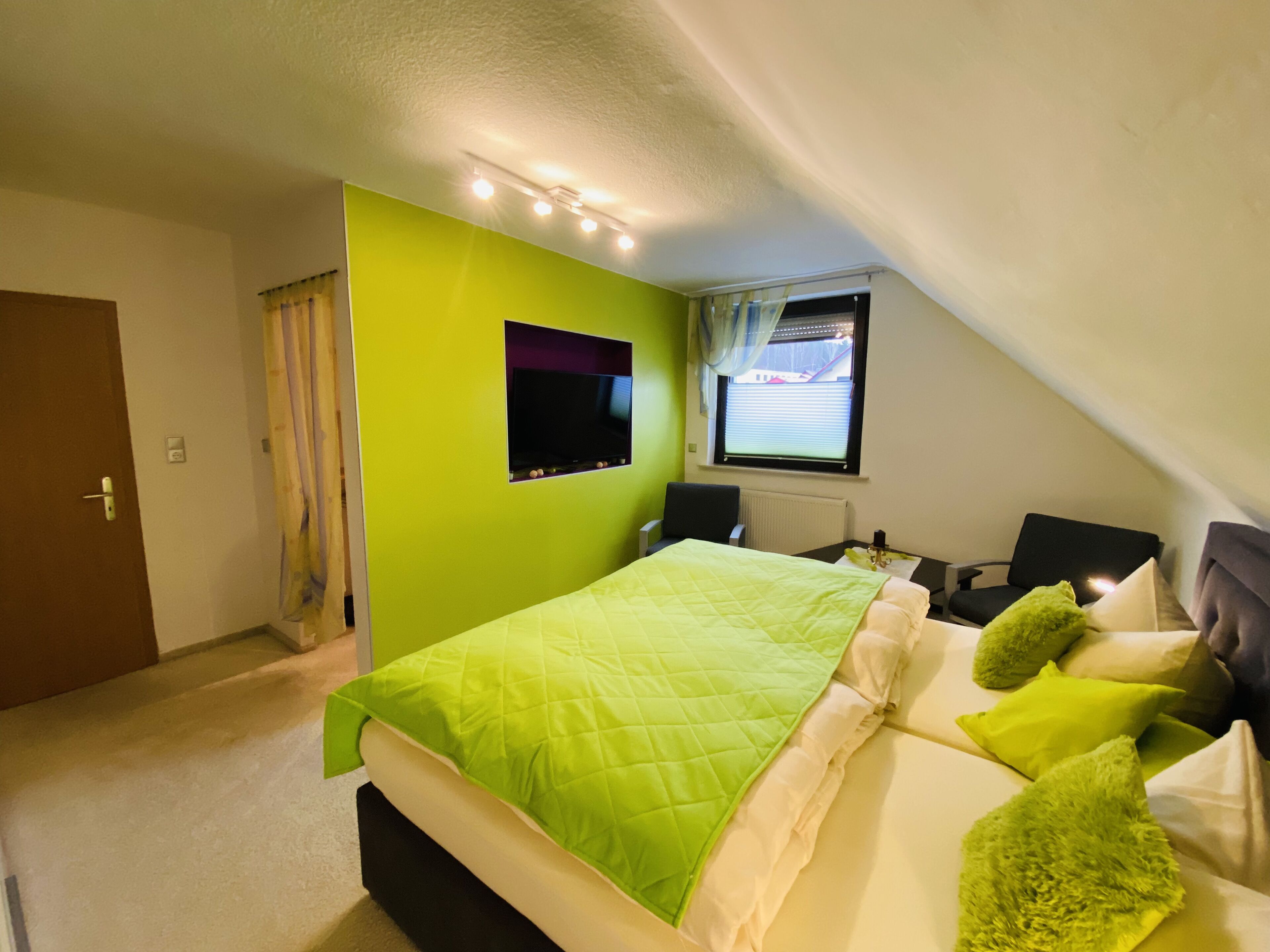 A bedroom with a bed, a window, a chair, and a television.