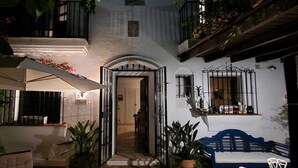 A courtyard with a covered seating area, a door leading to a room, and potted plants.