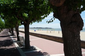 A tree-lined promenade leading to a beach with a soccer goal and people in the distance. - In Royan, Beautiful apartment 100 m from the beach and the city center with sea view (Royan)
