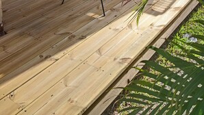 Um deck de madeira com cadeiras amarelas e uma mesa, cercado por vegetação.