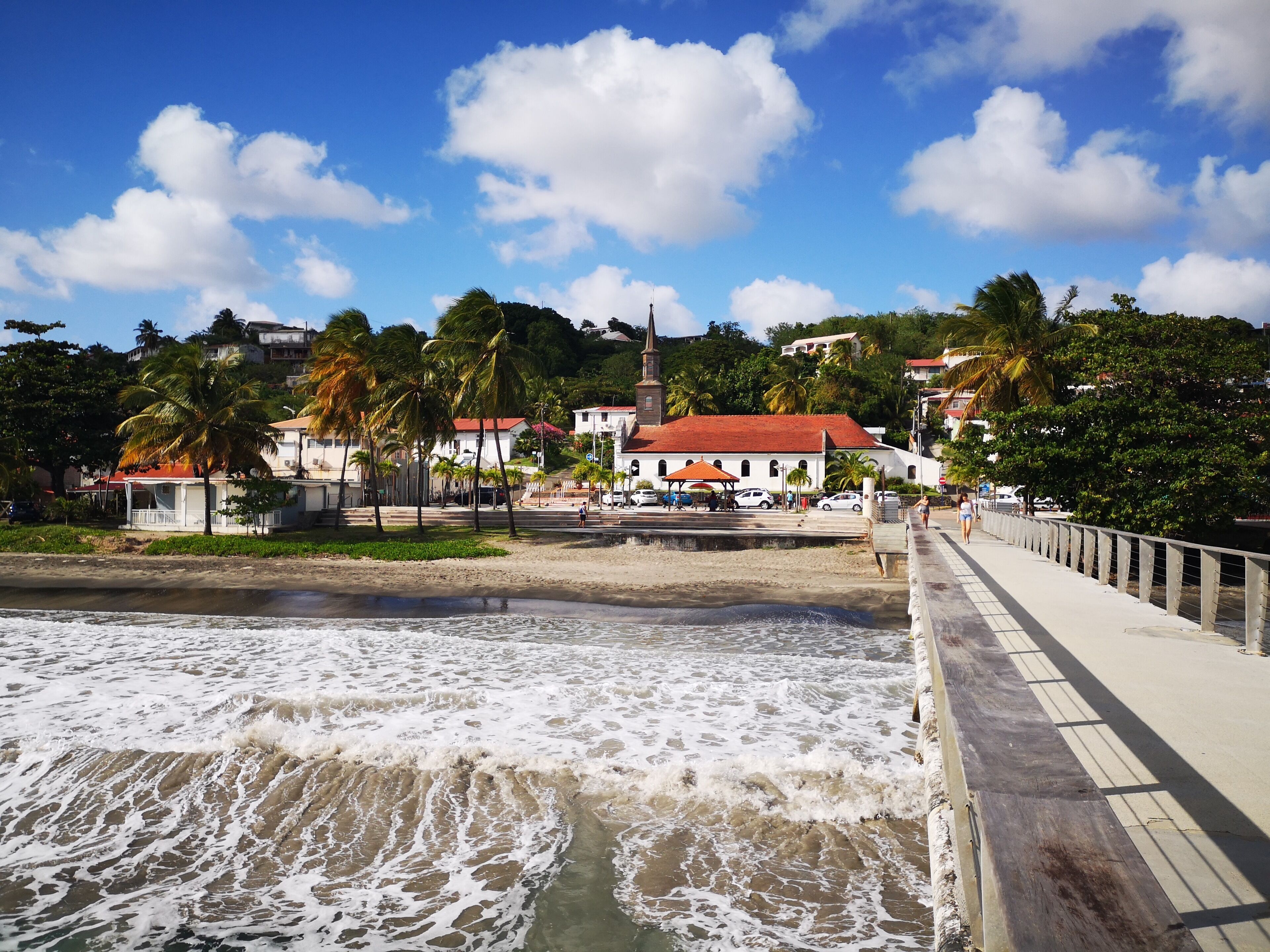 A coastal area with a beach, a pier, and buildings in the background.