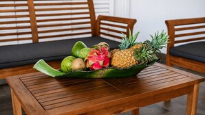A wooden table with a fruit bowl containing dragon fruit, pineapple, and other fruits. - Large villa **** beachfront with pool  (La Saline-Les-Bains)