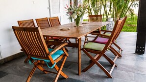 A wooden dining table with chairs, a vase of flowers, and a view of greenery outside. - Large villa **** beachfront with pool  (La Saline-Les-Bains)
