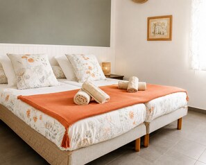 Un lit bien fait, avec une literie à motifs floraux, une serviette enroulée et un plaid orange.