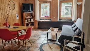 Une pièce chaleureuse avec un décor intérieur en bois, un canapé, une table à manger avec des chaises, un téléviseur et une fenêtre avec des rideaux.