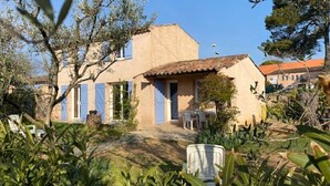 Uma casa com telhado de cerâmica, um jardim com plantas e uma porta azul.