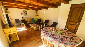 Um quarto aconchegante com teto de madeira, piso de azulejos, uma mesa de jantar com cadeiras, uma mesinha com abajur e uma porta.
