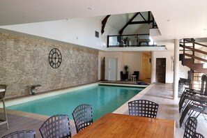 Una amplia piscina interior con pared de ladrillo y una mesa de madera con sillas.