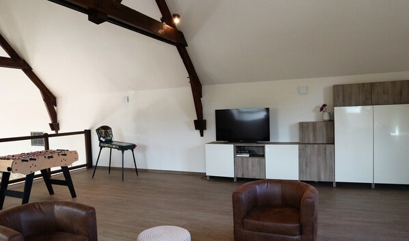 A spacious living area with a foosball table, a television, and a kitchen area with a refrigerator and cabinets.