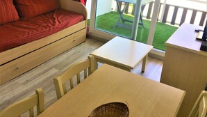 Ein gemütliches Zimmer mit einem roten Sofa, einem kleinen Esstisch mit Stühlen und einer Glastür, die auf einen Außenbereich mit einer Holzterrasse führt.