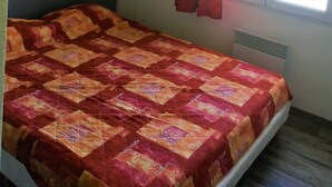 Ein Schlafzimmer mit Bett, Fenster mit Vorhängen, einem Wandbild und einem Heizkörper.