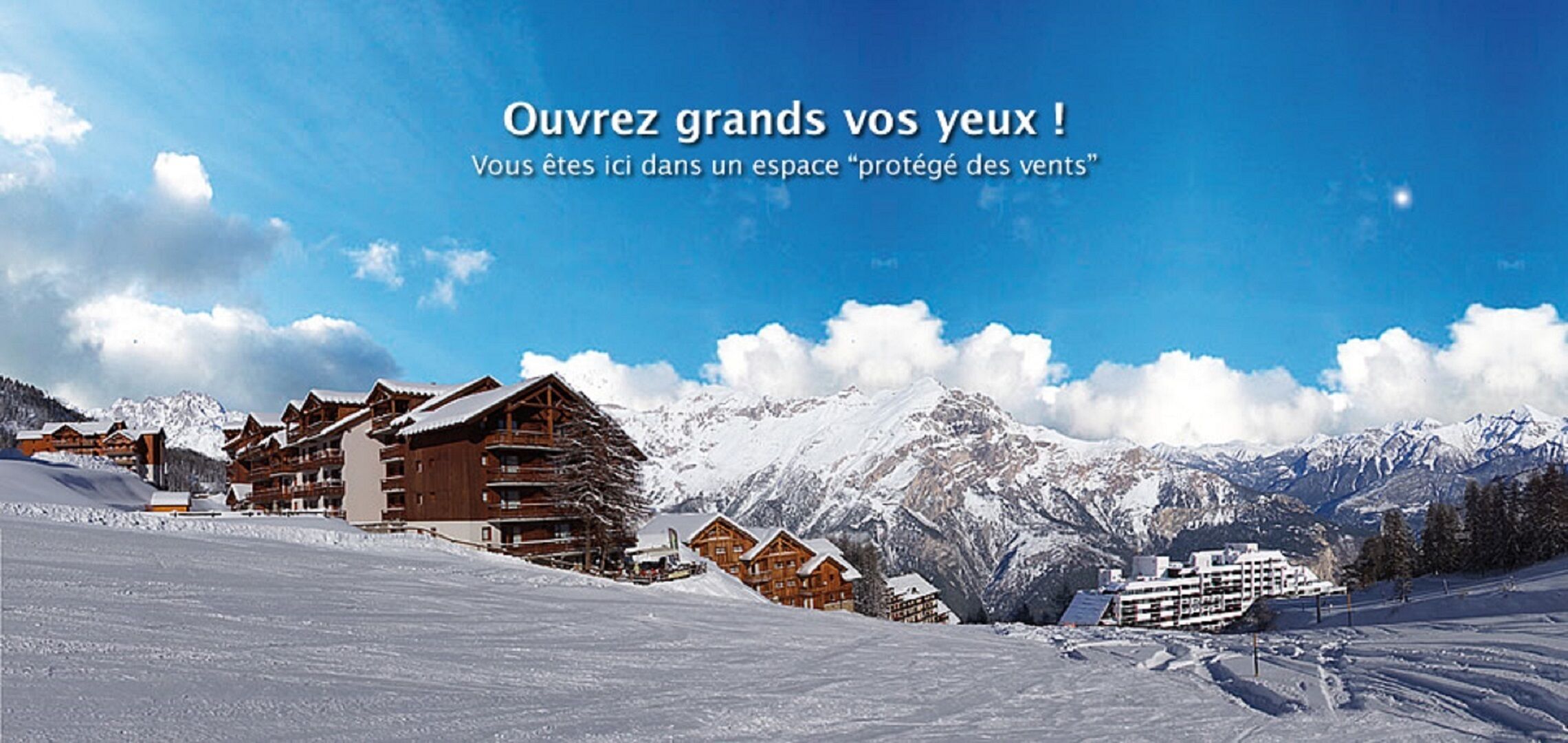 Estância de esqui com montanhas cobertas de neve, chalés de madeira e um céu azul límpido.