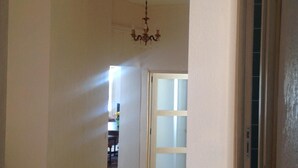 A hallway with a chandelier, a door with frosted glass panels, and a view into another room.