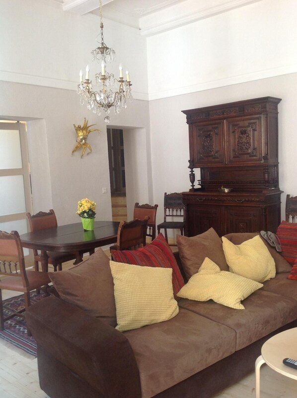 A living room with a brown sofa, a dining table, and a chandelier.