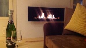 A living room with a flat-screen TV mounted on the wall displaying a fireplace, a bottle of champagne, and two glasses on a wooden table.
