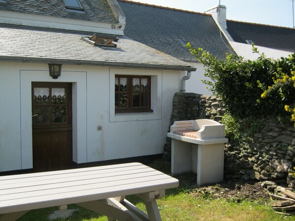 A white cottage with a stone wall, a wooden door, and a window with a decorative frame. - CHARMING LITTLE HOUSE Belliloise (Sauzon)