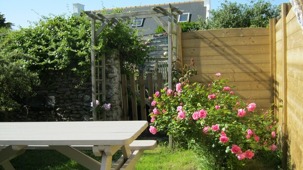 A picnic table in a garden with a wooden fence, a climbing plant, and a stone wall in the background. - CHARMING LITTLE HOUSE Belliloise  (Sauzon)