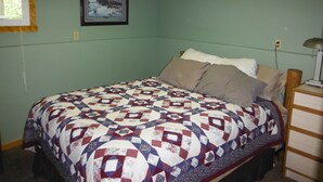 Une chambre à coucher avec un lit, une table de chevet, une lampe, un tableau encadré au mur et une fenêtre avec un rideau.