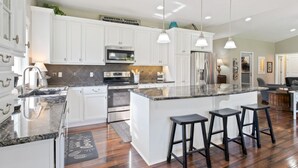 A modern kitchen with white cabinets, a large island with bar stools, stainless steel appliances, and pendant lighting. - HUGE, 10 BEDS, FAMILIES, REUNIONS & RETREATS! LAKE FUN 1 MILE-FREE POOL PASSES! (Omaha)