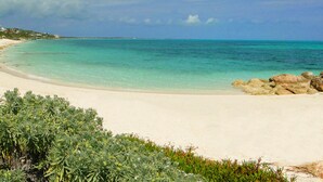 A beach with clear turquoise water, sandy shore, and rocky outcrops.