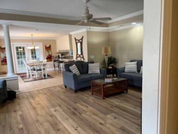 A spacious living room with a wooden floor, two sofas, a coffee table, and a ceiling fan.
