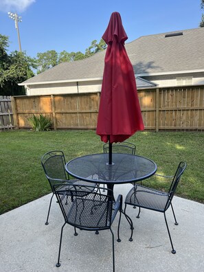 A round metal table with four chairs and a red umbrella in a backyard.