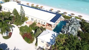 Vista aérea de un complejo turístico con piscina, sombrillas de playa y paneles solares.
