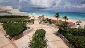 A resort with a paved walkway leading to a beach, surrounded by landscaped areas and palm trees.