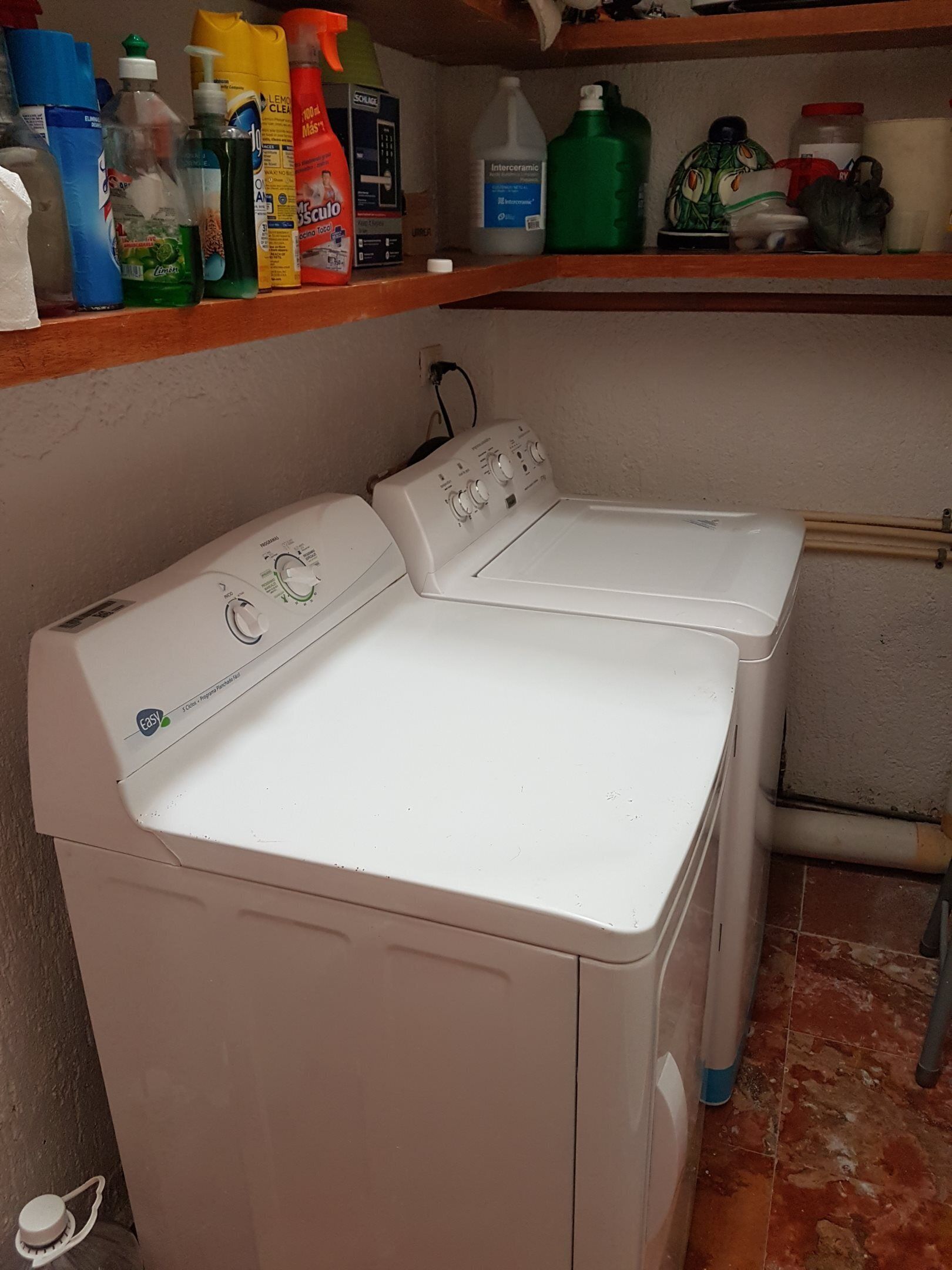 A front-loading washing machine with a control panel, a shelf above with cleaning supplies, and a tiled floor.