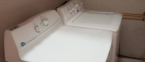 A front-loading washing machine with a control panel, a shelf above with cleaning supplies, and a tiled floor.