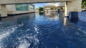 A swimming pool with a stone bridge, modern buildings, and clear skies.
