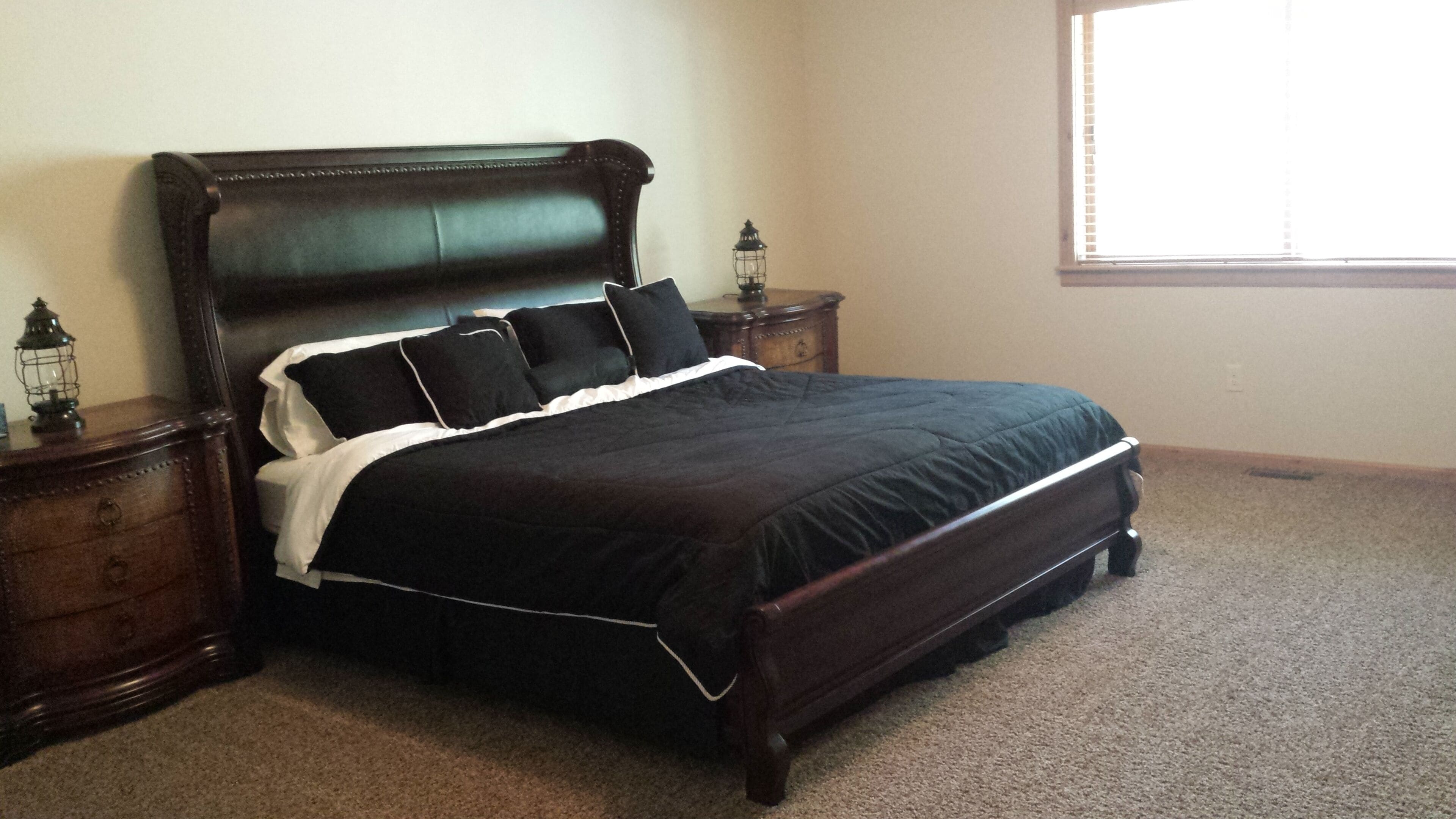 A bedroom with a large bed, wooden headboard, two nightstands, and a window with blinds.