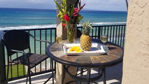 Een tafel met een ananas, een glas witte wijn en een bord met fruit, met uitzicht op de oceaan.
