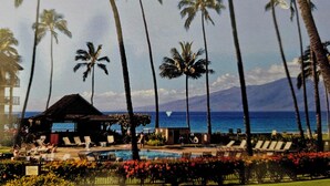 Een resort met een zwembad, ligbedden, palmbomen en uitzicht op de oceaan.
