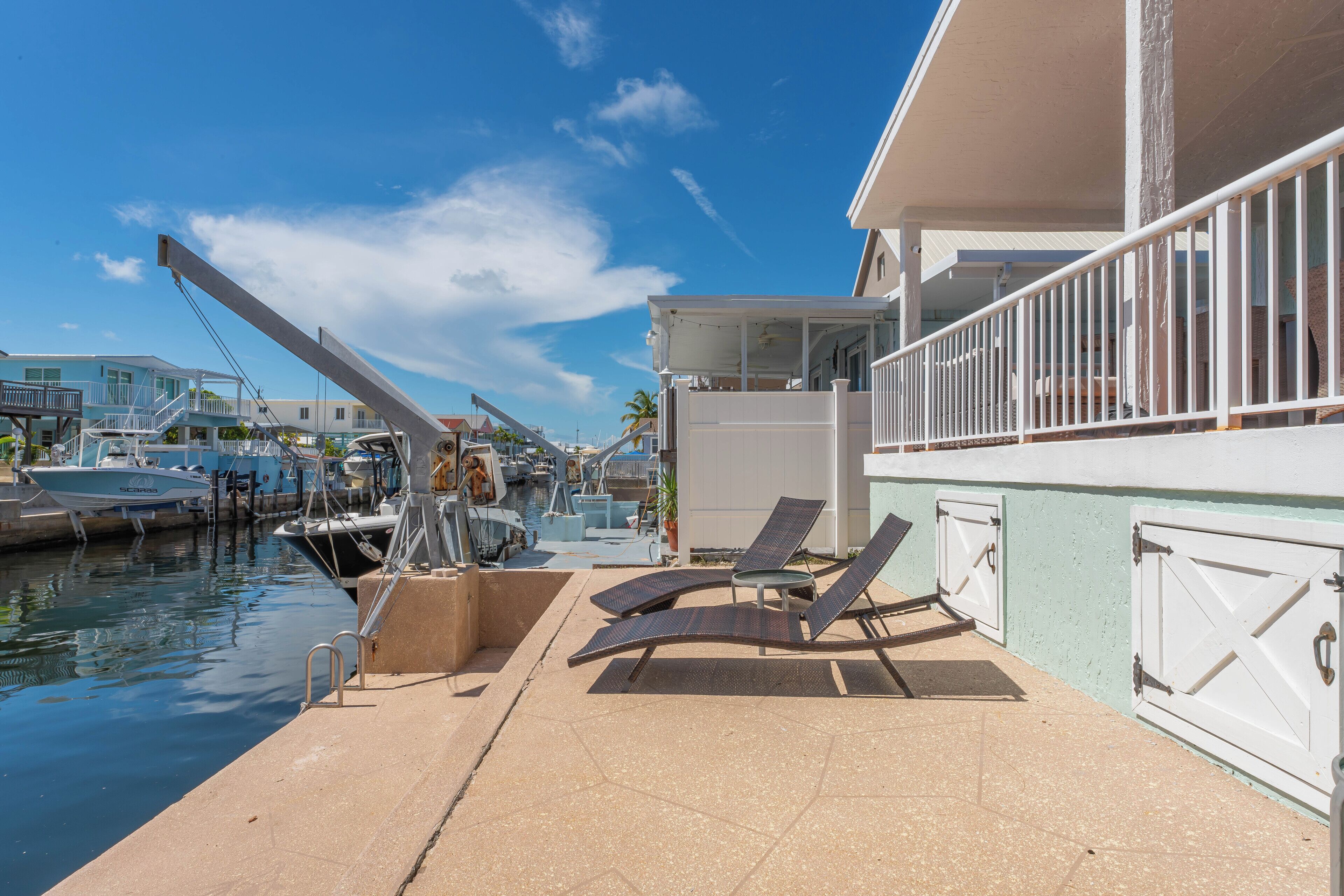 A marina with boats docked, a covered area with lounge chairs, and a building with a balcony.