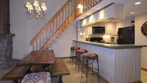 Une cuisine avec un escalier en bois, une table à manger avec des bancs et un coin bar.