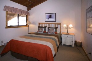 A bedroom with a bed, bedside lamps, a nightstand, a framed picture on the wall, and a window with a valance.