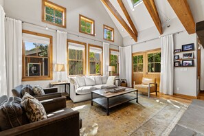A spacious living room with a high ceiling, large windows, and a cozy seating area.