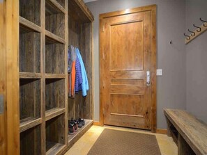 A wooden door with a bench, a shoe rack with shoes, and a coat rack with jackets.