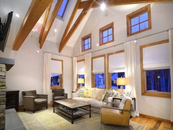 A spacious living room with a high ceiling, large windows, and a cozy seating area.