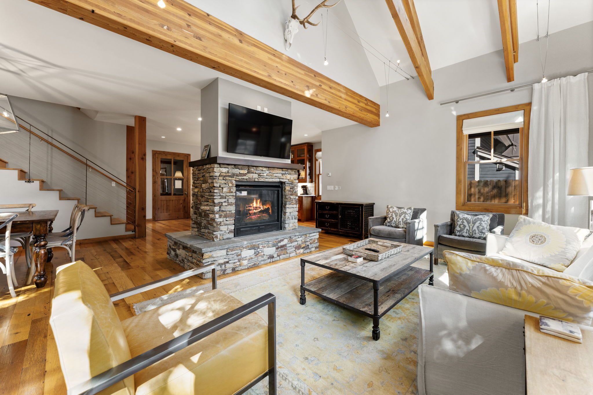 Ein geräumiges Wohnzimmer mit Kamin aus Stein, Holzbalken, einem Flachbildfernseher und einer Treppe, die zu einer weiteren Ebene führt.