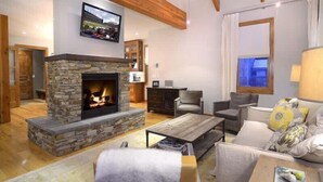 A cozy living room with a stone fireplace, wooden beams, a television, and comfortable seating.