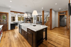 A modern kitchen with a central island, wooden flooring, and a stone fireplace.