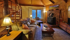 L’intérieur chaleureux d’un chalet avec un escalier en bois, une cheminée, un canapé et une table à manger.